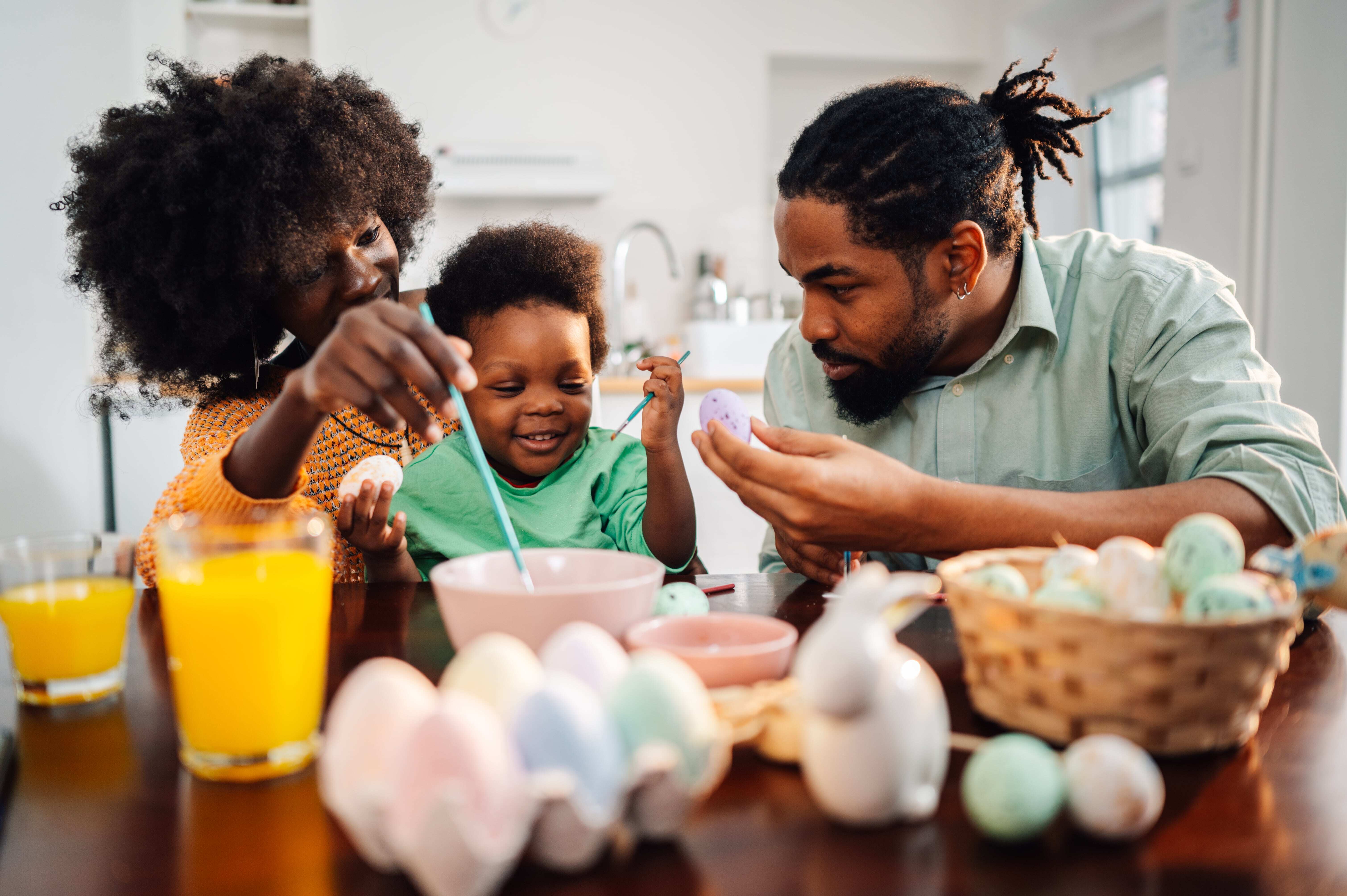 A young family sitting at the breakfast table painting Easter eggs and enjoying kid-friendly recipes.  