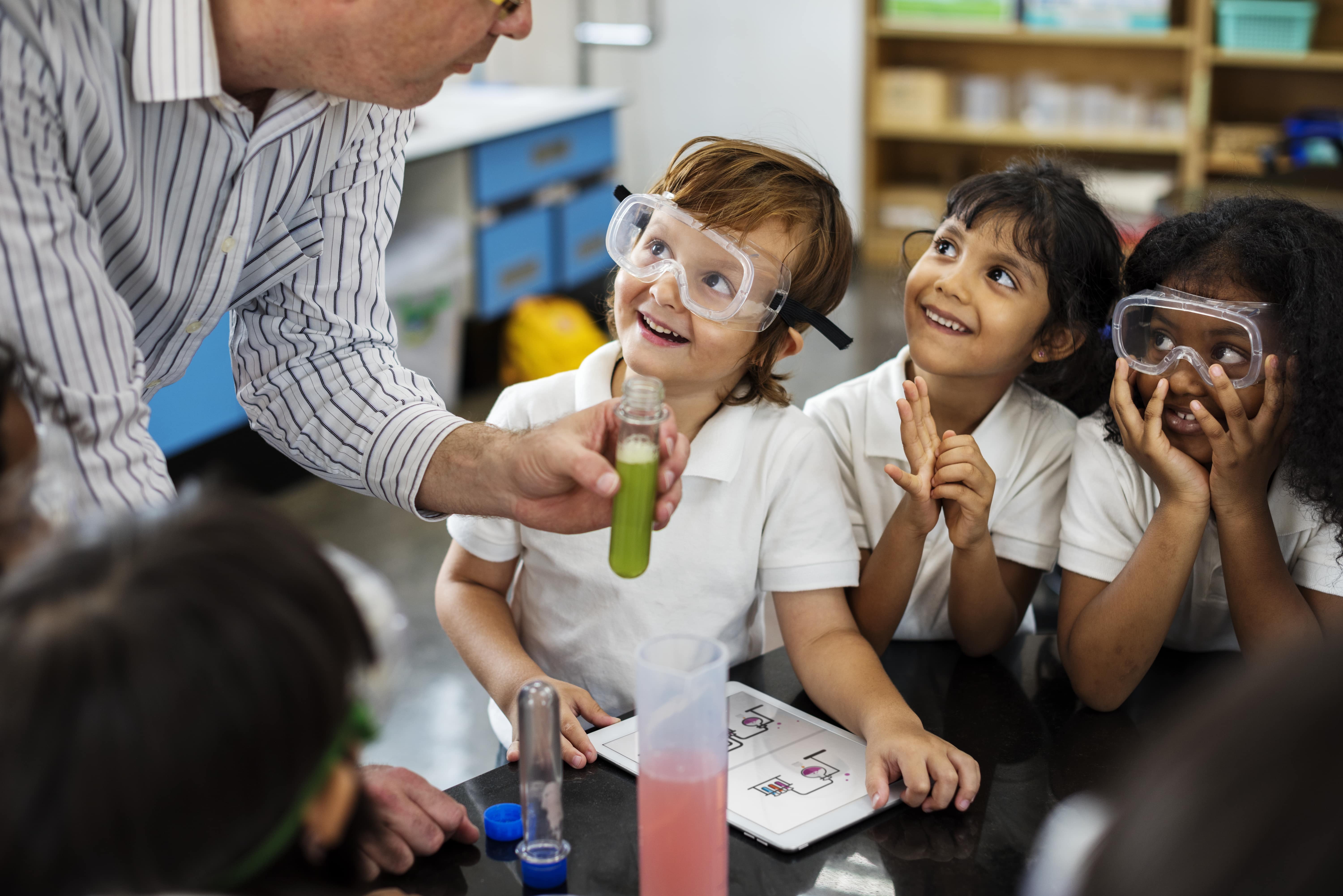 Young children looking up at their educator with admiration as they prepare to do a science experiment and learn about STEM concepts. 